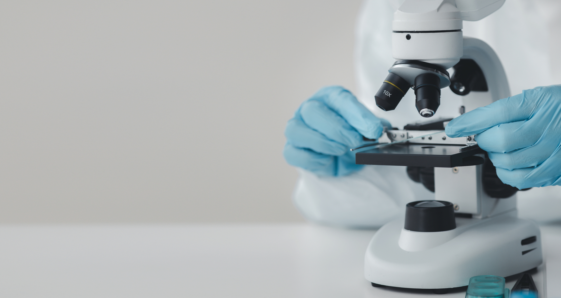 Research microscope Close up of someone wearing a lab coat and blue latex gloves using a microscope.